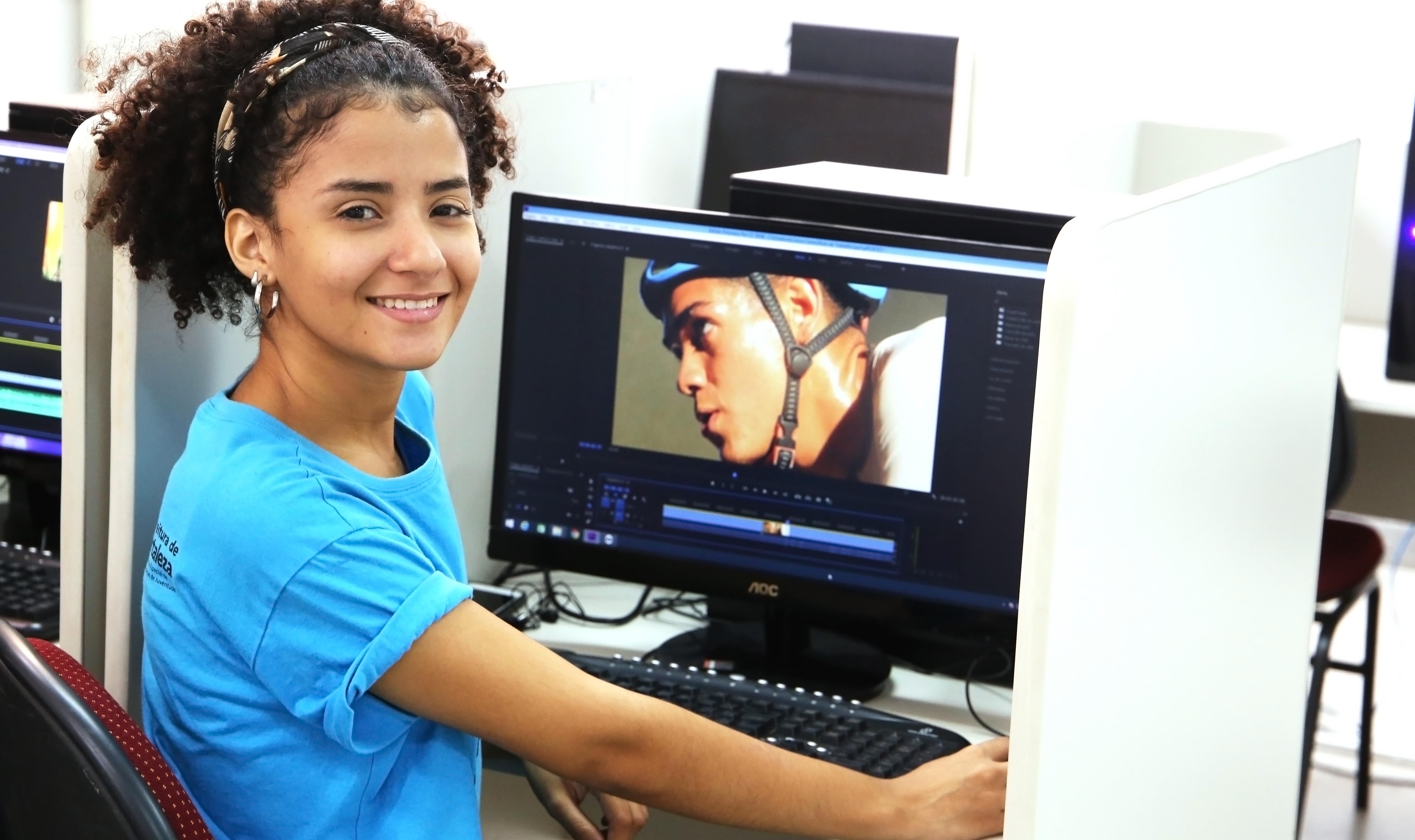 garota sorrindo para a foto em frente a computador enquanto edita foto
